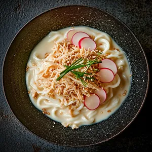 The dish presents a harmonious tapestry of color and texture; white noodles coated with glossy sauce, generously sprinkled with crescent-shaped radish slices that inject a vibrant red rim. A pile of shredded chicken imbued with the warmth of ginger, Chives and sesame seeds add the finishing touch to this masterpiece.