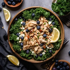 The plate is filled with a bed of curly kale leaves topped with shredded pulled chicken, toasted almonds, crumbled feta cheese and clusters of plump blueberries.