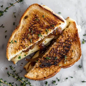 From above, you see a symmetric, golden toasted sandwich. Cutting diagonally, it reveals layers of creamy cheese along with the glossy caramelized onion jewel-tones and glimpses of deep purple fig jam. A sprinkle of fresh thyme on the top adds a subtle pop of green and the oozy brie is just waiting to be pulled apart.