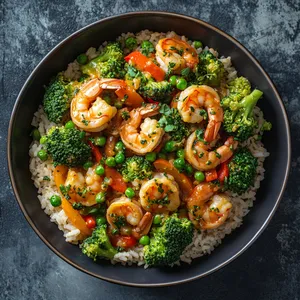 A vibrant medley of fresh, steamed broccoli florets, plump shrimp, and crisp bell peppers shine in their saucy splendor against a backdrop of warm, fluffy rice. The dish is generously scattered with fresh herbs and orbs of green peas for an extra burst of color.