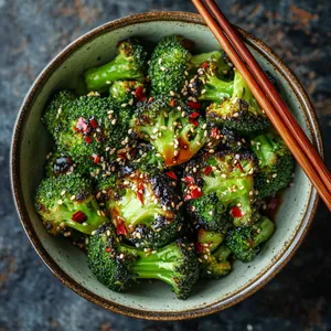 Emerald florets of broccoli charred to perfection, arranged majestically in a beautiful ceramic bowl. The dish is speckled with fiery red pepper flakes and glossy sesame seeds, brightened by a vibrant and glossy citrus Ponzu drizzle. An optional pair of designer wooden chopsticks adds an extra 'click' for Instagram.