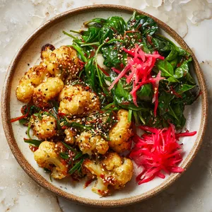 Imagine a plate adorned with mounds of grilled golden-brown, crisp cauliflower florets, glossed with a shiny ginger-soy sauce. It's brilliantly contrasted by the vibrant green of a seasonal spinach salad on the side. Sprinkles of sesame seeds and dollops of julienne pickled ginger introduce poppy reds and whites for a stunning panorama of colors and textures.