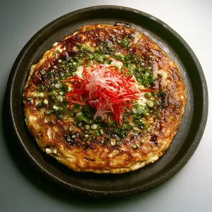 On a stoneware plate, imagine a round, golden-brown pancake, tender centers topped with dazzling green spring onions, glossy red strips of pickled ginger, a drizzle of the creamy mayonnaise and the sticky brown Okonomiyaki sauce. A final sprinkling of fluttering bonito flakes completes the picturesque plate.