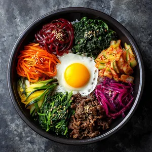 From above, it's a beautiful mosaic of multi-colored ingredients symmetrically arranged around a sunny yolk of a fresh egg nestled in the center. The white bed of rice lays the canvas for the vibrant green of seasoned spinach, royal purple of shredded beetroot, punchy orange of julienned carrots, and the brownish charm of the bulgogi meat. A colorful assortment of Banchan dishes adds to the tapestry.