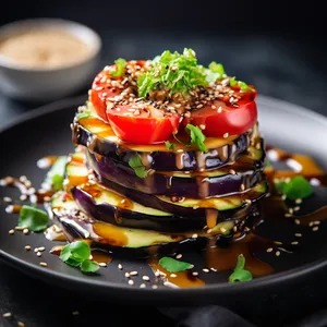 Layers of golden crispy eggplant slices stacked with vibrant avocado, juicy tomatoes, and a drizzle of tangy sesame dressing.