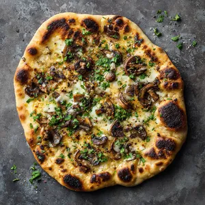 A golden-brown, hand-formed disk of dough, speckled with bits of earthy Cremini mushrooms. The bread has an appealing irregular shape, with rustic, charred spots from baking, and strands of melted mozzarella lightly pulled apart. A Sprinkle of fresh, green chopped cilantro on top gives it a pop of color and vibrancy.