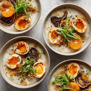 From above, four shallow bowls of pale, silky congee are topped with halved marbled soy tea eggs, deeply browned oyster mushrooms, a small tuft of bright tangerine-herb salad, scattered black sesame seeds, emerald scallions, and golden garlic chips glistening in chili oil.