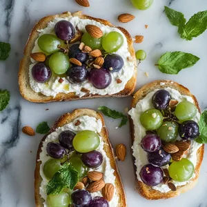 A beautiful cacophony of purple and green grapes adorning golden toast, with ricotta providing a milky white backdrop, interspersed with golden brown roasted almond pieces. Fresh mint leaves add a beautiful crowning green touch.