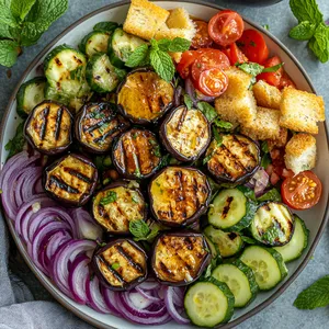 Vibrant purple circles of grilled eggplant fill the base of the plate. An array of diced cucumbers, cherry tomatoes halved and red onions lends a lively color contrast. A golden drizzle of honey lemon vinaigrette dresses the top of the salad. Croutons are sprinkled around, with a final garnish of fresh mint leaves.