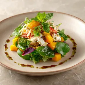 A vibrant medley of colors and textures, with the bright orange of the crab and mango, the verdant green of the mint and baby spinach, and the rich earth tones of the spices and vinaigrette. The salad is elegantly presented on a neutral palette plate, accentuating the colorful, heaped salad.