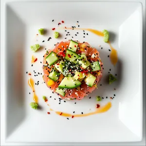 The top view shows a circular mold of tuna tartare at the center of a square white plate, vibrant with colors from the red tuna, the green avocado and cucumber, and the golden sesame seeds, specks of red chili and black sesame seeds scattered on top. Delicate drizzles of miso dressing artistically arc around the tartare, with small dots of wasabi mayo, signifying an bonafide culinary art piece.