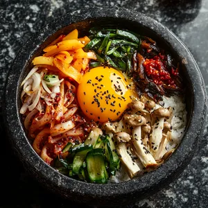 A hot sizzling stone pot contains a vibrant medley of colors: finely sliced rainbow-colored vegetables, creamy yolk of a sunny-side-up egg, dark brown sautéed Cremini mushrooms, and specks of white rice peeking out. On the side, a small dish of deep-red gochujang paste waits to be mixed in, adding a splash of thrilling color.