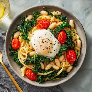 Creamy burrata melting over a bed of linguini, topped with vibrant green sautéed kale, plump white cannellini beans, and bright red cherry tomatoes. A zest of lemon and a final sprinkle of pepper adds a culinary finish.