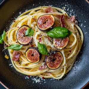 A visually stunning plate of twirled lemony linguine, with deliciously charred fig halves and crispy prosciutto shards scattered about. The garnish of fresh basil leaves adds a pop of green, and tiny specks of red chili give a hint of heat. The pasta is dusted with finely grated Parmesan, providing a lovely white contrast against the colorful backdrop.