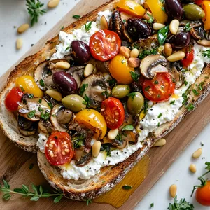 The vibrant colors of the ripe heirloom tomatoes, deep purple Kalamata olives, and fresh green thyme leaves pop against the creamy white backdrop of ricotta and oyster mushrooms, garnished with a drizzle of golden honey. It's decorated with toasted pine nuts for a final crunch, served on a rustic, wood board.