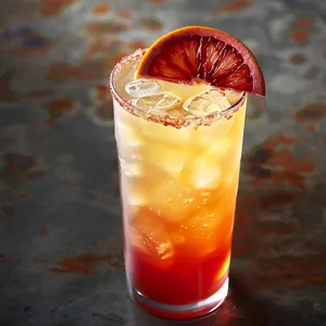 The cocktail, served in a tall hurricane glass, is crowned with a thin slice of wheel-cut blood orange. The bubbles gently rise up, capturing the shades of a New York sunset: crimson on the bottom, gradually transitioning to golden orange, then a hint of paler orange, creating an ombre effect.
