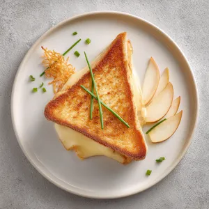 From above, the sandwich is cut diagonally and slightly overlapped on a matte white plate, revealing a glossy pull of melted cheese. The bread is deeply golden with lacy crisp edges, topped with a delicate shard of parmesan frico standing upright like a skyline. A small swoosh of onion jam, scattered chive batons, and a few thin apple fan slices make the plate look polished, modern, and celebratory.