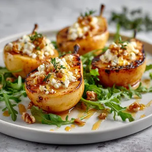 Four halves of caramelized, grilled pears sit on a white plate, their concaves filled with a mash of rich, marinated feta cheese. Sprinkles of thyme and crushed walnuts scatter the surface. A drizzle of golden honey zigzags across the pears creating a visually enticing pattern. Around the base of pears, fresh arugula leaves garnish the plate, offering a vibrant contrast.