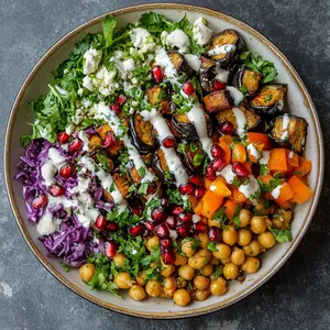 A vibrant plate layered with colorful greens, purples, oranges, and whites from the falafel, salad, and tahini drizzle. The majesty of the roasted eggplant crowned with the scatter of pomegranate seeds, mint, and a drizzle of ruby red pomegranate molasses is a sight to behold.