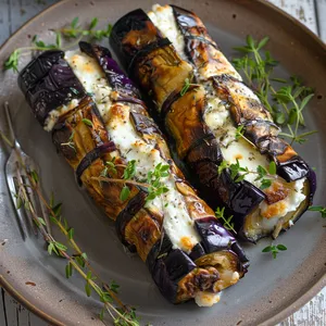 Two glistening eggplant roulades lay cozied up on a rustic ceramic plate. The deep purple of the eggplant skin is complemented by the creamy white of the goat cheese peeping out from the scroll. Fresh herbs scatter over the top, lending the dish a pop of vibrant green.