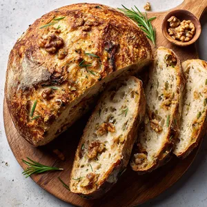 A round, crusty loaf, perfectly golden and crisp on the outside. As we cut open the loaf, the fluffy, steamy inside reveals morsels of earthy celery root and bits of toasted walnuts. The vibrant green specks of rosemary add a sprinkling of rustic charm.