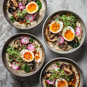 From above, four shallow bowls of pale creamy oats are topped with halved jammy eggs, glossy caramel-brown mushrooms, ribbons of vivid green sorrel, pink radish slices, black and white sesame seeds, chili oil swirls, and tiny herb leaves for a striking, modern brunch look.