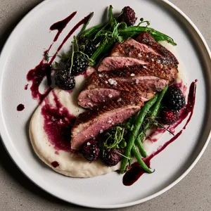 From above, two sliced duck breasts fan across pale ivory purée, surrounded by glossy emerald haricots verts, jewel-toned blackberries, and artistic streaks of deep plum thyme jus, finished with microgreens and flaky salt on a matte white plate.