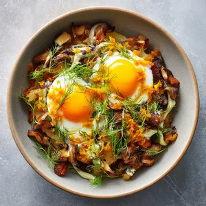 A radiant dish of varying textures and colors: a warmly toasted fennel hash as the foundation, topped by two glistening egg yolks, studded with shiitake bacon bits and a splash of vibrant orange citrus zest. Strands of fennel fronds add a touch of delicate green, while a drizzle of honey-tinged sour cream crisscrosses the dish.