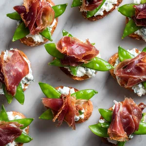 Vibrant green snow peas rest atop a snow white bed of creamy goat cheese nestled on thin slices of deep rosy crispy prosciutto. Each ingredient contrasting the other in a visual and flavorful dance.