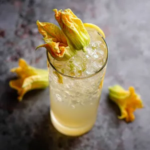 An enchanting drink in a tall glass, with the bright citrusy clear cocktail punctuated by floating ice cubes. Garnished with the dainty yellow squash blossoms and a twist of lemon peel, it's truly an Instagram-ready sight.
