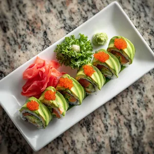 From above, the sushi roll resembles the statue of liberty's torch, with expertly layered fish, avocado, and cucumber, wrapped in vibrant green nori and studded with dazzling 'flame'-made from bright orange tobiko. Served on a white rectangular plate with a side of vibrant pink pickled ginger and light green wasabi to contrast the sushi roll’s colours.