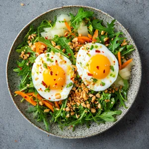 Emerald Arugula forms bed beneath two softly poached eggs, their rich yellow yolks still dripping. Surrounding are mounds of daikon and carrot pickles, the bright colors contrasting beautifully. The dish is sprinkled with crushed peanuts and dabs of chili-lime dressing for a vibrant splash of color, a visual feast before the first delicious bite.