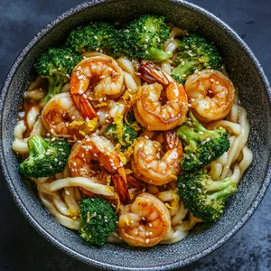 Creamy, yet vibrant udon noodles served in a deep bowl. The caramelized shrimps are enticingly scattered among the bright green broccoli florets. Yuzu zest and sesame seeds are finely sprinkled on the top, providing a final touch of visual flair.